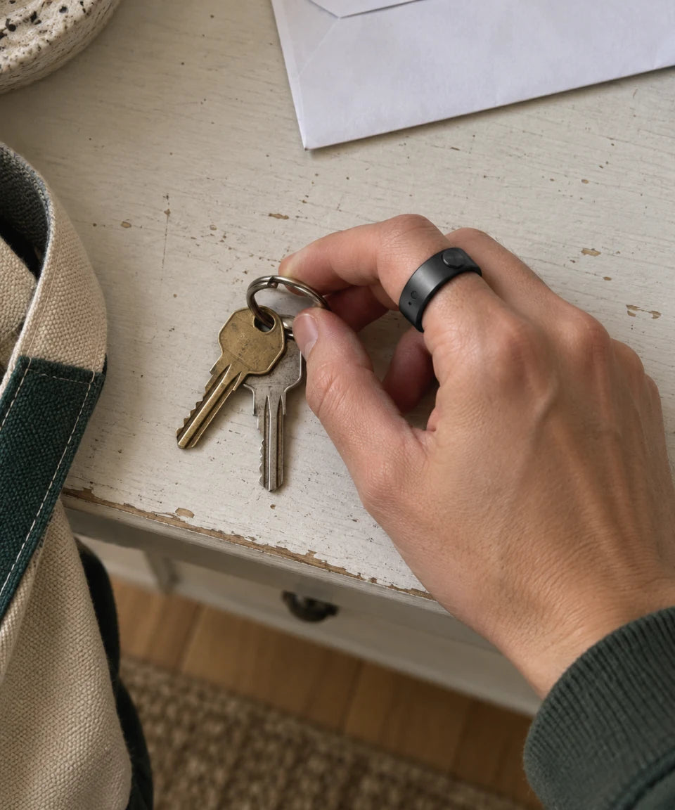 Illustrative close-up: a hand wearing the Secondly ring picks up house keys.