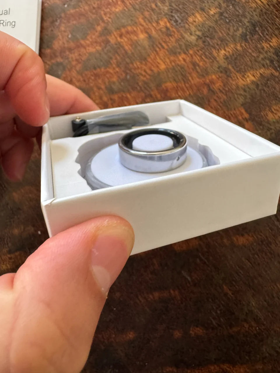 A close view of a silver Secondly ring resting in its open box.
