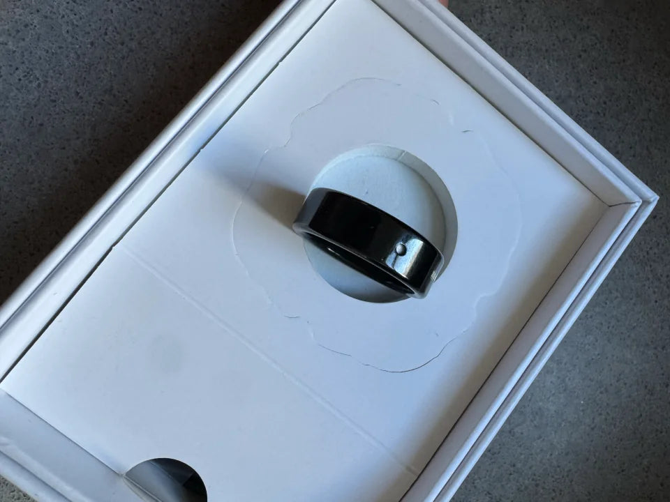 A black Secondly ring in its open white box, with the button visible.